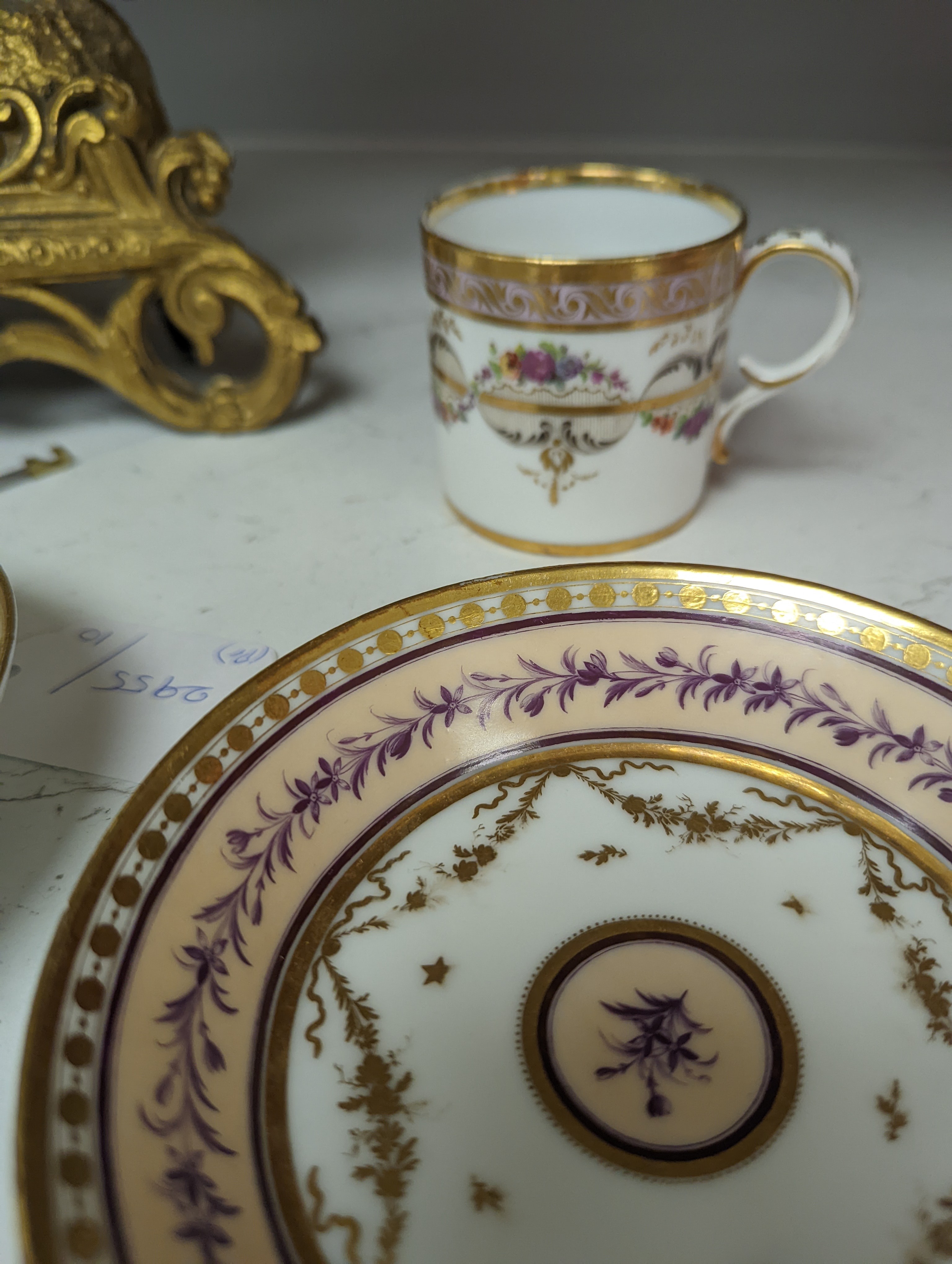 A Duc d'Angouleme coffee can and saucer painted with a puce chain of leaves on a salmon coloured ground and another painted with a flower chain, black feather and a gilt line, latter with stencilled red mark 'Manuf de M